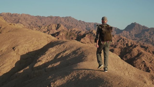 Senior male traveler walking on a desert rock with selfie stick handheld shot