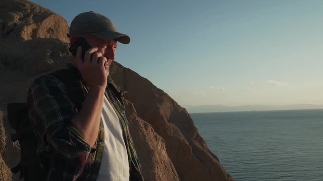 Handsome senior male traveler speaking by smartphone in mountains handheld shot