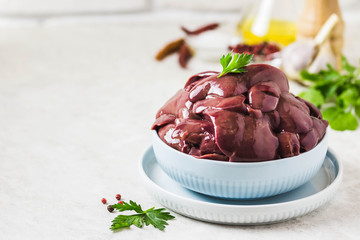 Raw chicken liver in a plate, pepper, herbs, oil. Selective focus, space for text.
