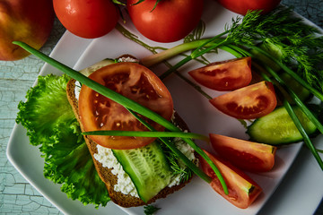 sandwich with cheese and sliced tomato cucumbers, lying on a white plate, decorated with green onions, standing on the old wooden table