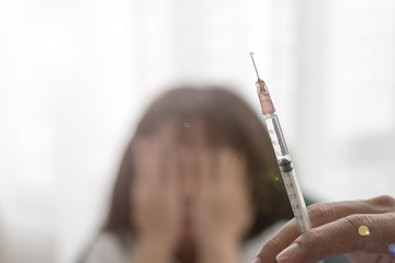  Vaccination concept. Hand of Doctor pediatrician holding vaccine syringe in hospital with blurred background of scary Asian kid girl hands on her face closing eyes with lens flare effect.