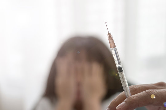 Vaccination concept. Hand of Doctor pediatrician holding vaccine syringe in hospital with blurred background of scary Asian kid girl hands on her face closing eyes with lens flare effect.