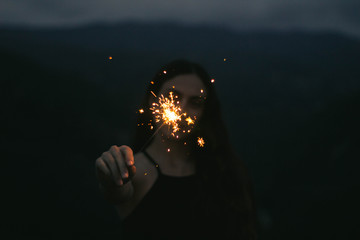 woman holding a sparkler in front of her night scenery in the top of a mountain