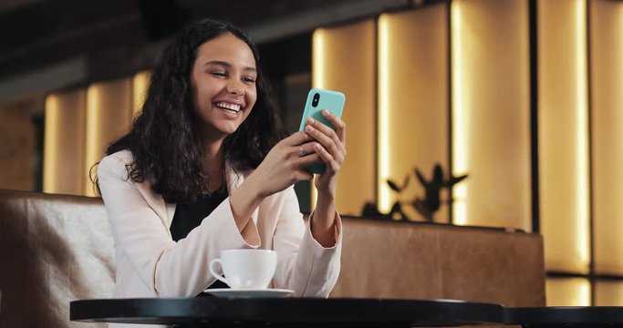 Business woman using smartphone in cafe drinking coffee laughing in cafe. Communication, successful business, dating, good mood concept
