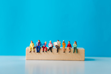 Miniature people sitting on wooden block with on blue background using as business and social concept