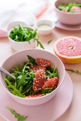 Fresh citrus salad with arugula, grapefruit and sesame seeds on pink background. Selective  focus. Raw vegetarian spring detox food.