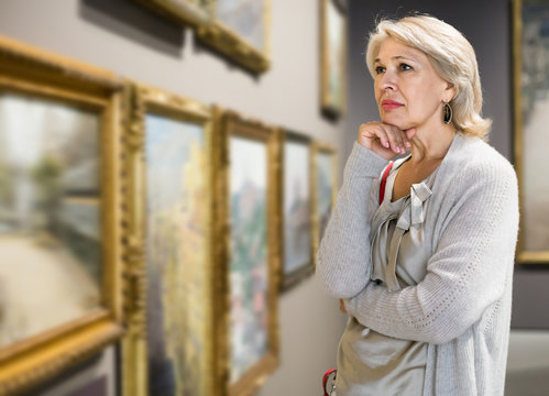 Mature woman standing in art museum near the painting in baguette