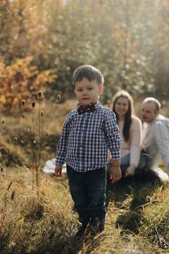 Portrait of stylish litle boy. His parents in banground. Child in shirt with bowtie