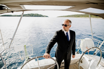 Gentleman mit Anzug am Steuer eines Segelbootes
