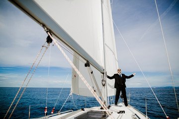 Mann mit Anzug jubelt auf einem Boot unter Segeln
