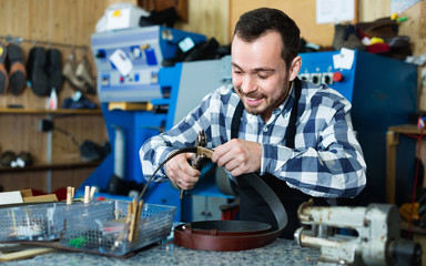 Male worker making hole in belt in specialized workshop