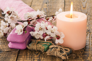 Soap with towel for bathroom procedures and burning candle with flowering branch of apricot tree