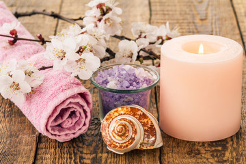 Fototapeta na wymiar Sea salt in glass bowl with towel for bathroom procedures, sea shell and burning candle with flowering branch of apricot tree