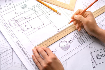 Girl architect draws a plan, graph, design, geometric shapes by pencil on large sheet of paper at office desk. Soft focus