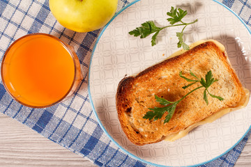 Toast with butter and cheese on white plate, apple and glass of orange juice.