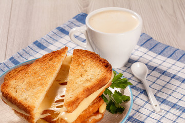 Toasted slices of bread with cheese and green parsley on white plate, cup of coffee and spoon on napkin.