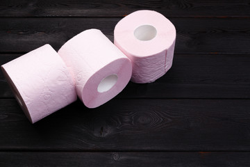 Pastel pink toilet paper rolls on black wooden background