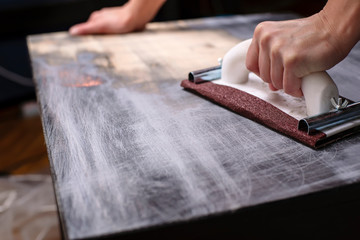 person prepares the surface for painting and sanding by hands an old wooden black table with a...