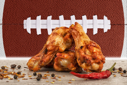 Chicken wings with red hot chili pepper, salt and peppercorn. Football ball image in background.