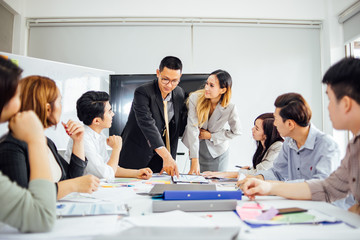 Businesswoman presenting to colleagues at a meeting.Successful team leader and business owner leading informal in-house business meeting. Businessman working on laptop in foreground.