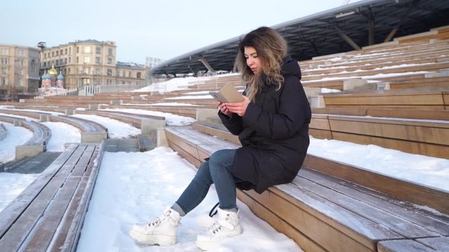 Delighted young woman reading asms on her mobile phone smiling with excitement at the good news as she stands outdoors