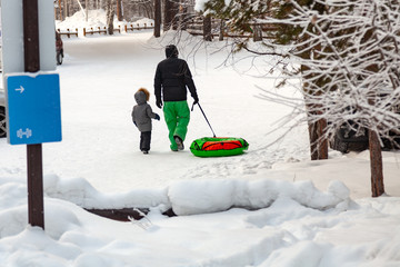 The man in green pants with their son spend the weekend in the woods go for a drive on the hill and pull the sleds behind them in an air chamber - tubing, on a frosty winter day.