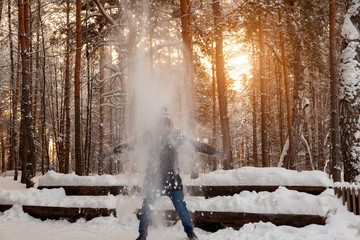 A man in the winter in the forest plays with snow, stands under a tree and shakes off the snow, covers it like an avalanche, from the branches with his arms spread across the breadth of his shoulders.