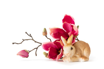 easter bunny sitting by some red magnolia flowers