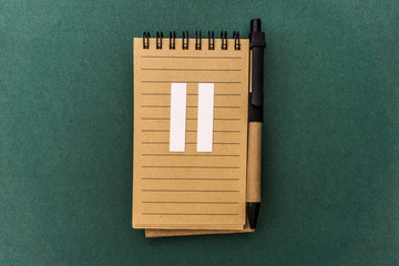 Notebook front with pen and white two Roman number on green background. Spiral notepad on a table....