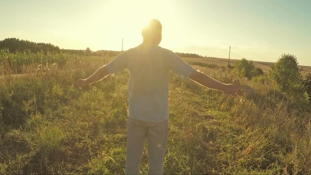 Man with arms raised looking at the rural landscape and enjoy the sunset. Slow motion