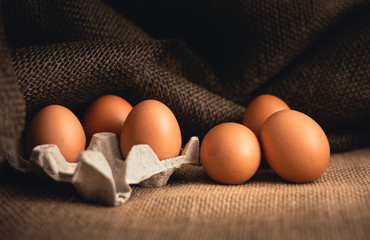 Photo of raw illuminated eggs  in kitchen with jute on dark background. Close-up photography of bio chicken eggs in egg box .