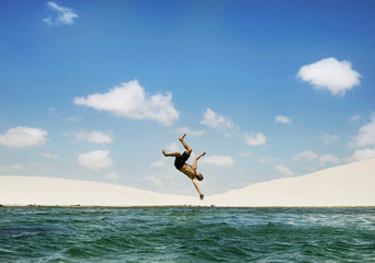 Man jumping backflip on lake with dunes in background, Lençois Maranhenses, Brazil