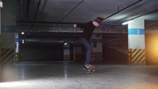 Underground parking lot. A young man skateboarding. Training his skills in kickflip trick