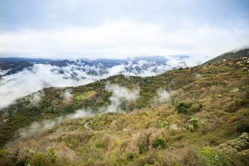 Panoramic top view of Alps mountains in fog and clouds, valley with clouds. Medieval buildings of Perinaldo town, Liguria, Italy