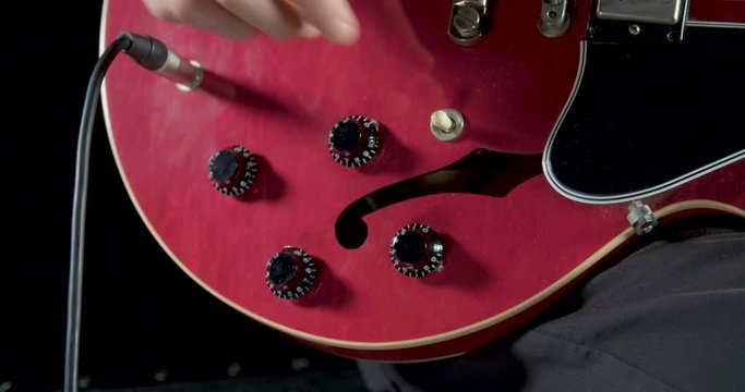 Man plugs jack cable into a guitar and adjust guitar knobs