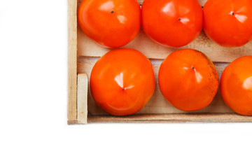 Juicy ripe persimmon in a large wooden box on a white background.