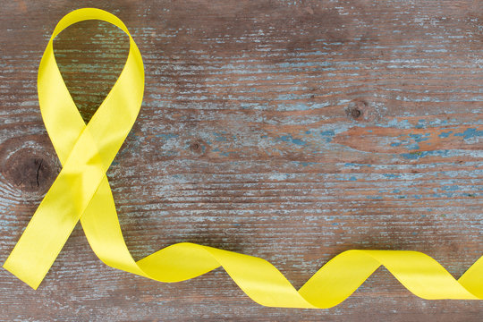 yellow ribbon-childhood cancer awareness symbol on the wooden background with copy space