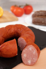 smoked sausages on a black plate with on a background of lemons and tomatoes and air black buns