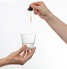 Closeup of hands holding eye dropper and a glass of water