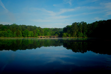 Fototapeta na wymiar Scenic view across the still water with mirror-like sky and tree reflections at Shelley Lake Park in Raleigh North Carolina.