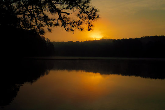 View of the rising sun peeking over the foggy horizon at Shelley Lake Park in Raleigh North Carolina.