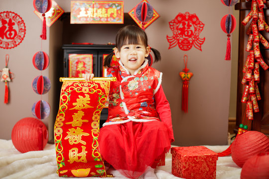 Chinese baby girl  traditional dressing up with a "Gong Xi Fa Cha" scrolls means "wishing you enlarge your wealth" against all kind of " FU" means" lucky" ornament and greeting card background