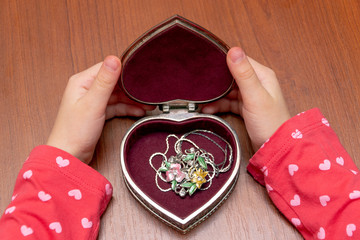 Opened old vintage silver heart-shaped casket in female hands on light coloured background