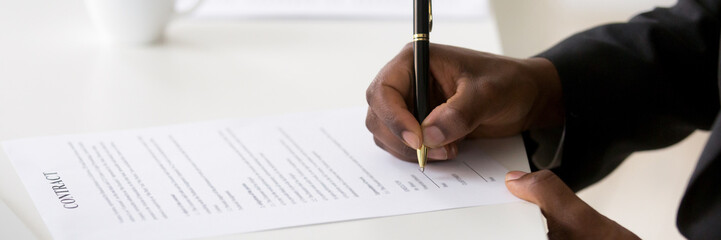 Horizontal photo close up black hired employee hands holds pen affirm contract paper with signature...