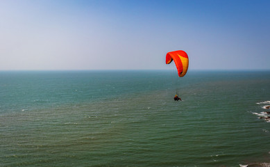 Paragliding in the sky. Paraglider tandem flying over the sea with blue water and mountains in bright sunny day. Aerial view of paraglider and Blue Lagoon in goa India at . Extreme sport. Landscape