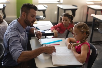 Young school teacher helping girl with study in classroom