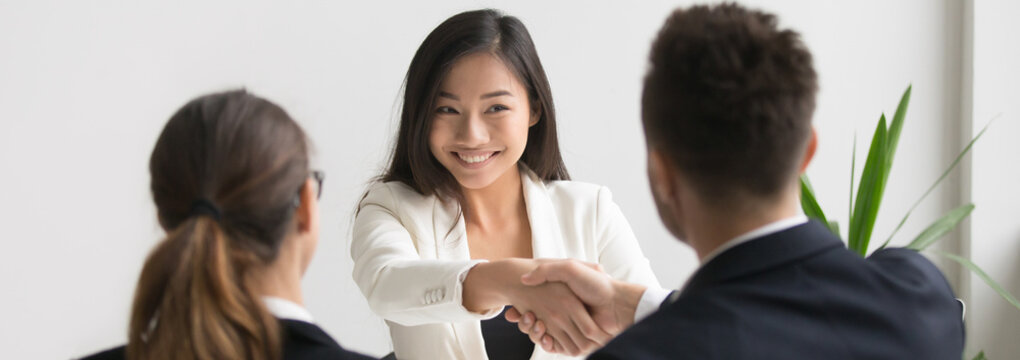 Smiling successful young asian applicant handshake with hr manager feels happy getting hired, boss congratulating employee new job employment concept. Horizontal photo banner for website header design