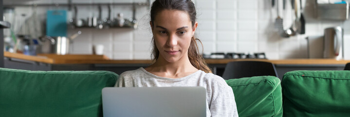 Horizontal photo focused mixed race woman sitting on couch at home using working on laptop reading...