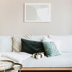 Modern interior design concept. Minimal Nordic Scandinavian style living room with photo frame on pastel beige wall, sofa with pillows and gift box. Comfortable apartment for rent.