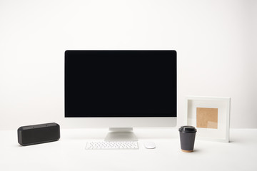 workplace with coffee to go, portable speaker and desktop computer with copy space isolated on white